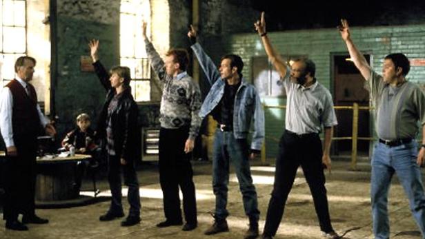 Eine Gruppe von Männern steht in einer Halle und hebt die Hände.