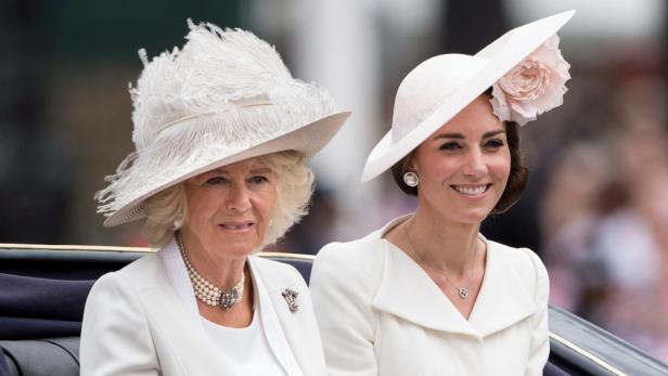 Camilla und Kate tragen elegante Hüte und helle Kleidung.
