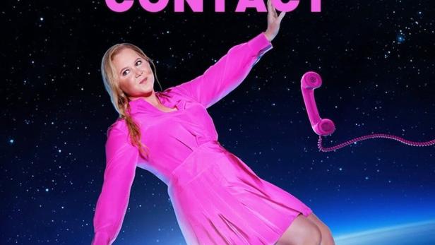 Amy Schumer schwebt im pinkfarbenen Kleid über der Erde, ein pinkes Telefon in der Hand.