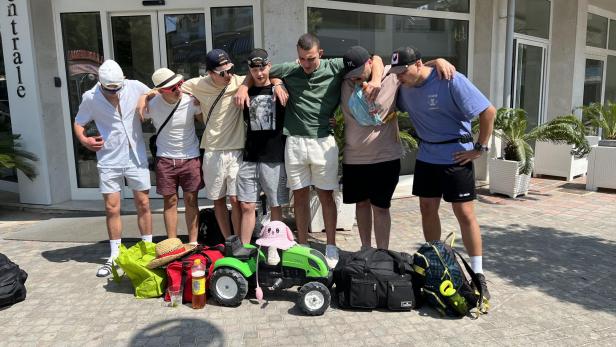 Eine Gruppe junger Männer steht vor einem Hotel mit Gepäck und einem Spielzeugtraktor.