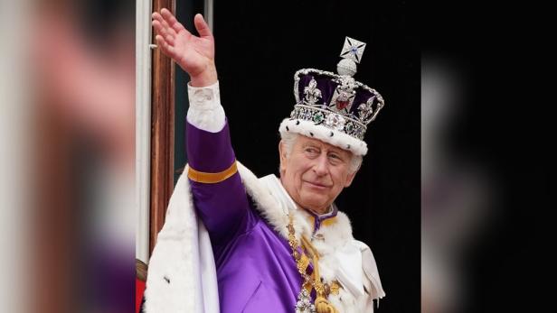 König Charles III. mit Krone und Hermelinmantel winkt.
