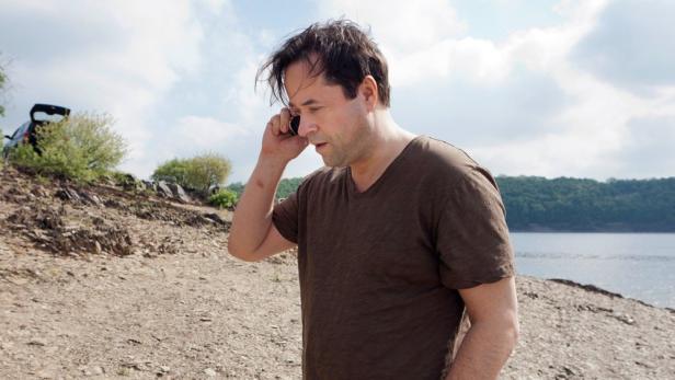 Ein Mann telefoniert am Ufer eines Sees.