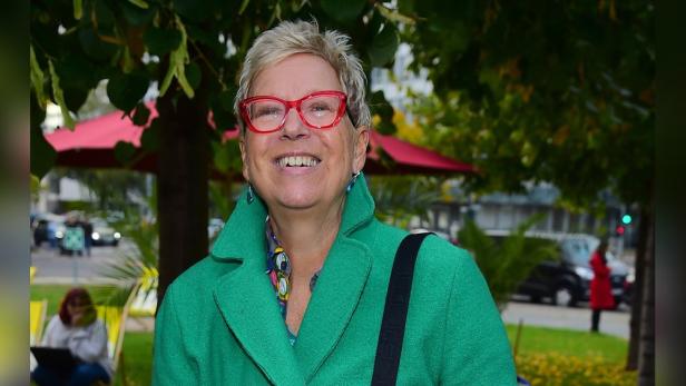 Doris Dörrie lächelt in einem grünen Mantel und roter Brille.