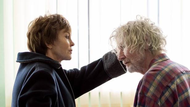 Eine Frau im Mantel spricht mit einem älteren Mann im karierten Hemd.