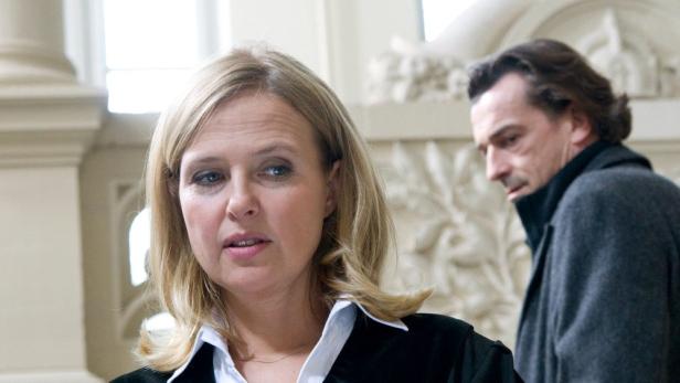 Eine Frau und ein Mann stehen in einem hellen Raum mit Stuckornamenten.