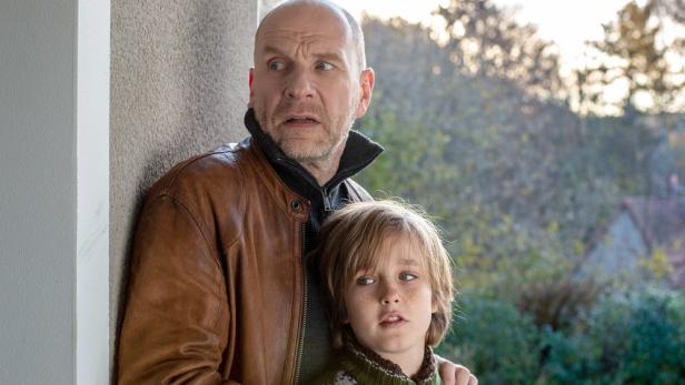 Ein Mann und ein Kind stehen ängstlich an einer Wand, möglicherweise in Gefahr.