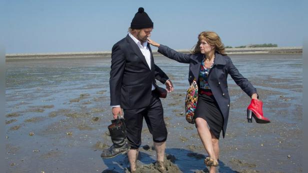 Ein Mann im Anzug und eine Frau mit Mantel stehen barfuß im Watt.