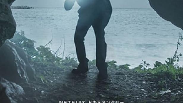 Ein Mann mit einer Taschenlampe steht am Eingang einer dunklen Höhle mit Blick auf das Meer.