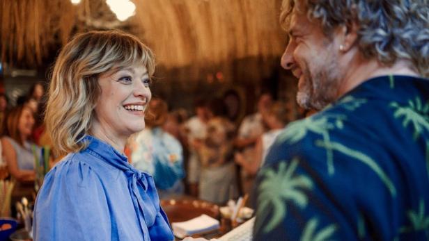 Eine lächelnde Frau unterhält sich mit einem Mann in einem Lokal, möglicherweise am Set von „König von Palma“.