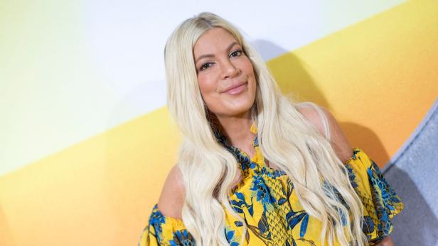Tori Spelling trägt ein gelbes Kleid mit blauem Blumenmuster.