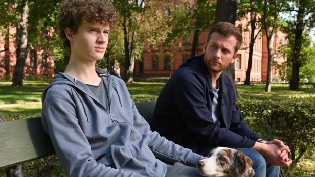 Ein Teenager und ein Mann sitzen mit einem Hund auf einer Parkbank.
