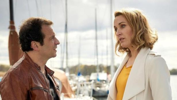 Ein Mann und eine Frau unterhalten sich vor einem Hafen mit Segelbooten.