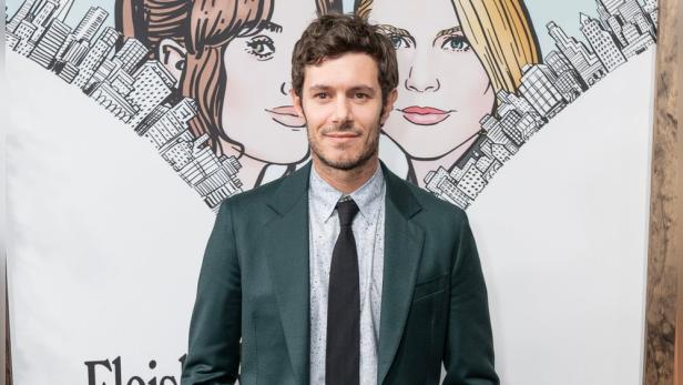 Adam Brody posiert vor einem Werbeplakat.