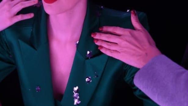 Eine Frau mit rotem Lippenstift und kurzem, blondem Haar trägt einen grünen Blazer.