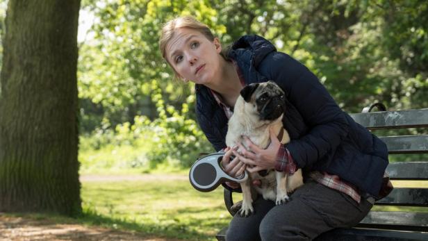Eine Frau sitzt mit einem Mops auf einer Parkbank.