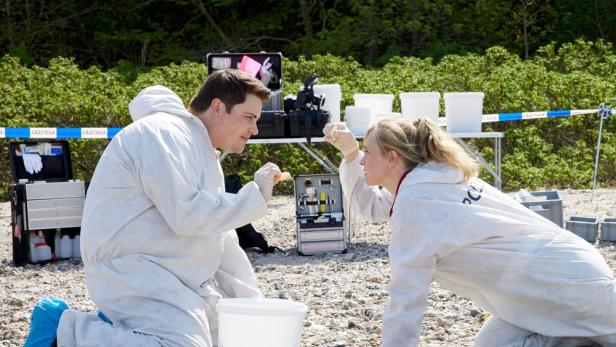 Zwei Spurensicherer in Schutzanzügen untersuchen ein Beweisstück am Tatort.