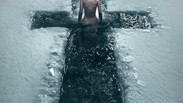 Eine Frau mit Tätowierungen steht in einem kreuzförmigen Loch im Eis, Titel „Deliver Us“.