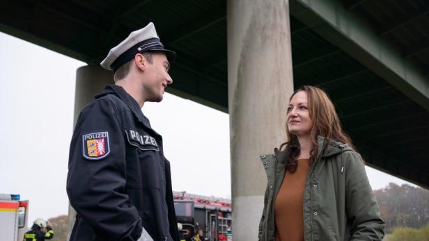 Ein Polizist spricht mit einer Frau unter einer Brücke; im Hintergrund ein Feuerwehrauto.