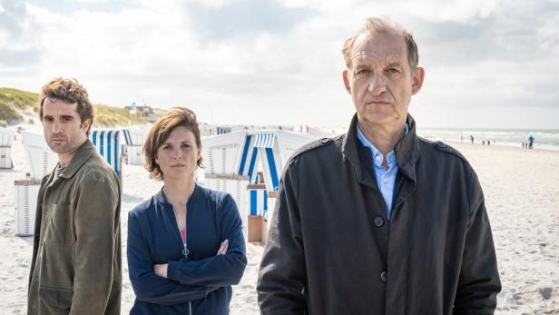 Die Schauspieler des deutschen Fernsehfilms „Nord Nord Mord“ stehen am Strand.
