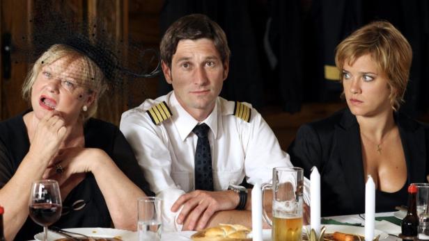 Drei Personen sitzen an einem Tisch bei einem formellen Abendessen.