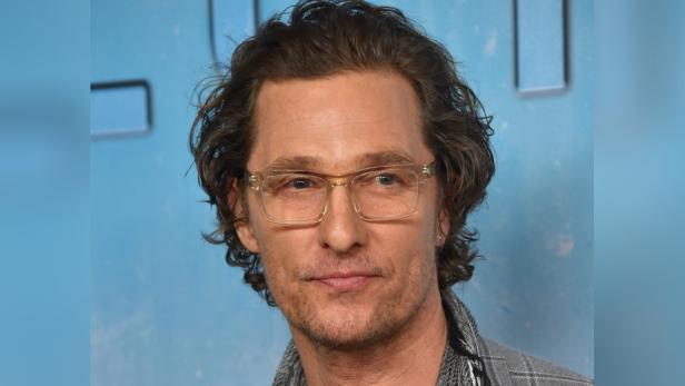 Porträt von Matthew McConaughey mit Brille vor einem hellblauen Hintergrund.