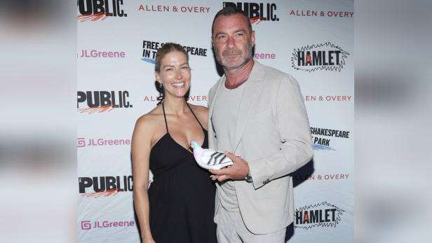 Liev Schreiber und seine Begleiterin posieren mit einer Taube vor einer Wand mit Sponsorenlogos.