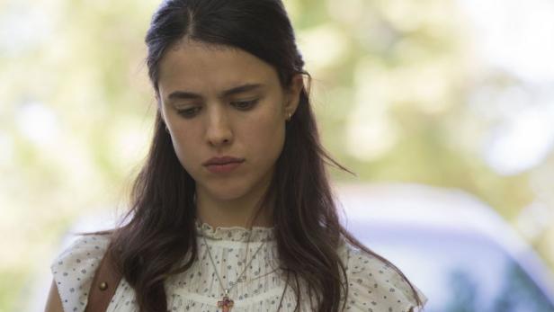 Eine junge Frau mit dunklen Haaren und einem Kreuz-Anhänger blickt nach unten.