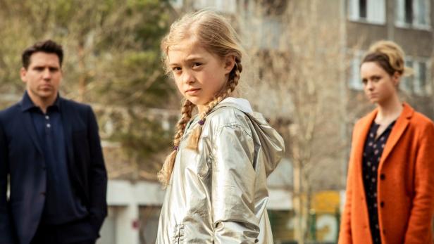 Ein junges Mädchen steht zwischen einem Mann und einer Frau.