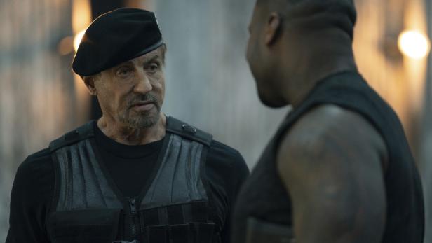 Sylvester Stallone in Kampfmontur spricht mit einem Mann.