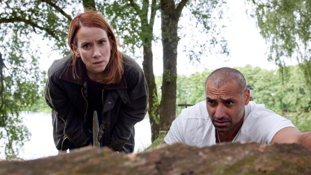 Zwei besorgte Personen, eine Frau und ein Mann, beugen sich über einen Baumstamm im Freien.