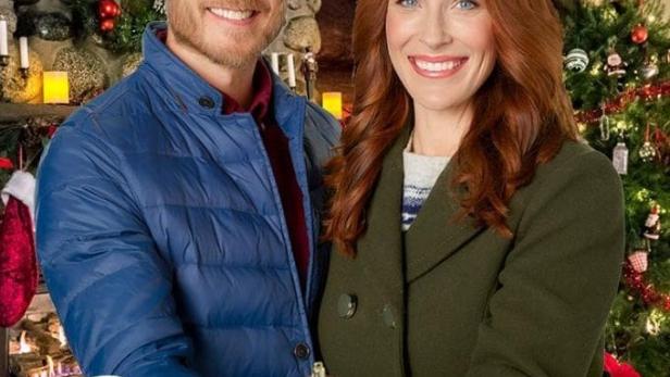 Ein Mann und eine Frau halten eine Christbaumkugel vor einem Weihnachtsbaum.