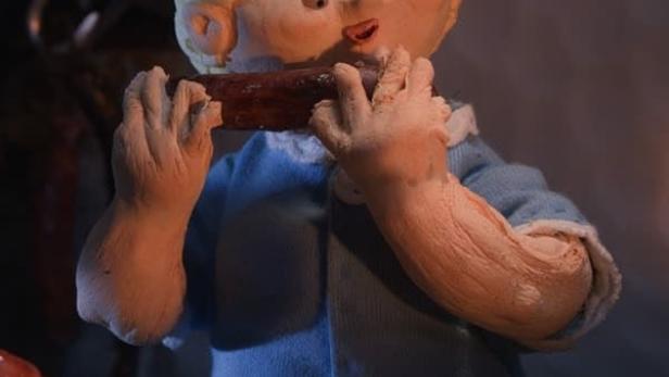 Eine Knetfiguren-Szene zeigt ein Kind, das eine Wurst isst, umgeben von weiteren Würsten.