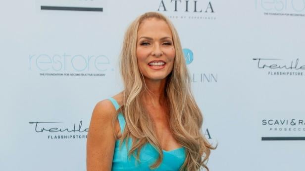 Eine Frau mit langen blonden Haaren in einem blauen Kleid vor einer Sponsorenwand.