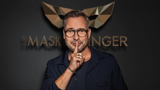 Matthias Opdenhövel posiert vor dem Logo von „The Masked Singer“ und bittet um Stille.