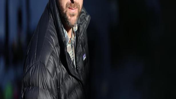 Ein Mann mit Bart und Mütze trägt eine schwarze Daunenjacke.