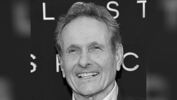 Schwarzweißporträt von Mark Goddard, lächelnd vor einer dunklen Kulisse.