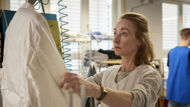 Eine Frau in Arbeitskleidung hängt ein weißes Kleidungsstück auf eine Maschine.