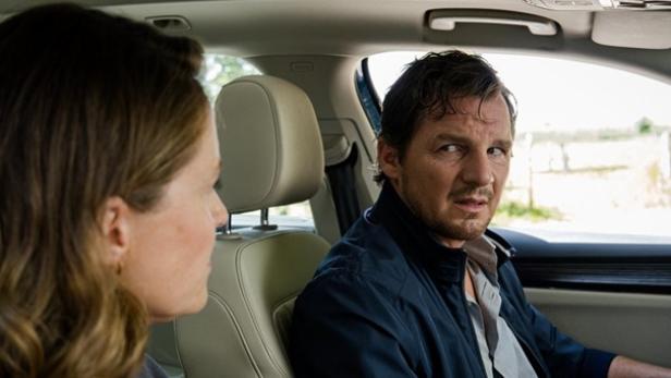 Ein Mann sitzt im Auto und schaut eine Frau an.