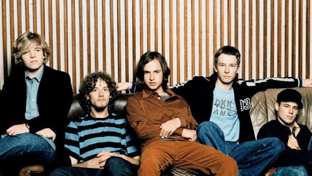 Die Band Echt sitzt auf einer Couch vor einer Wand mit Holzpaneelen.