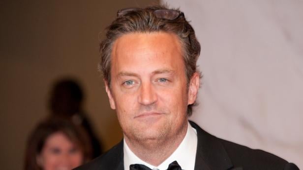 Ein Porträt von Matthew Perry in einem schwarzen Anzug.