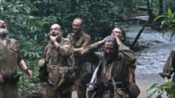 Eine Gruppe von Soldaten watet während eines Regengusses durch einen Fluss.