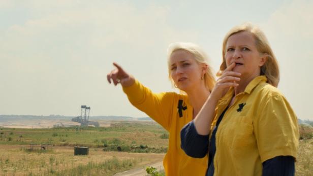 Zwei Frauen in gelber Kleidung stehen vor einer Tagebau-Landschaft.