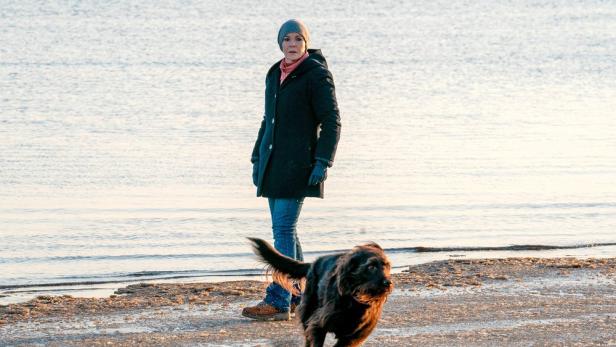 Eine Frau steht am Strand, während ein Hund auf sie zurennt.