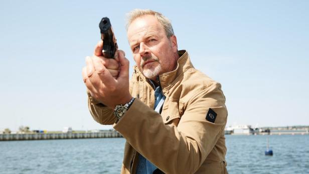 Ein Mann zielt mit einer Pistole vor einer Küstenlandschaft.