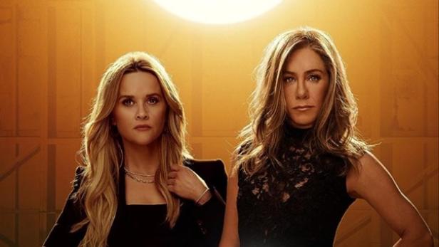 Reese Witherspoon und Jennifer Aniston in schicken Klamotten vor einer goldenen Wand