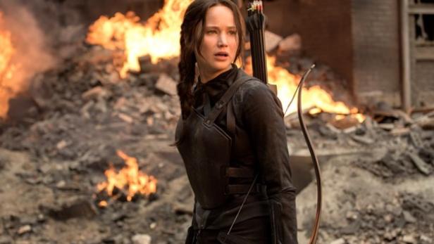 Jennifer Lawrence als Katniss Everdeen in einem schwarzen Outfit vor einem brennenden Haufen