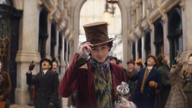 Timothée Chalamet in einem lila Anzug mit Hut in einer schicken Einkaufspassage