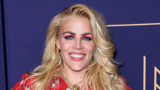 Busy Philipps mit blonden Haaren und auffälligem pink-grünem Augen-Make-up lächelt.