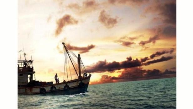 Ein Fischerboot fährt bei Sonnenuntergang auf dem Meer; im Vordergrund steht der Titel „Ghost Fleet“.
