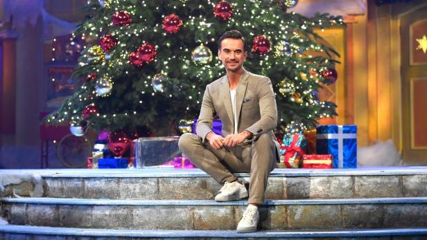 Ein Mann sitzt vor einem geschmückten Weihnachtsbaum auf einer Treppe.